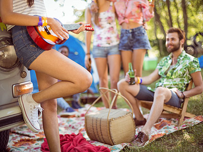 Eine Gruppe junger Menschen bei einem Picknick im Freien, einer spielt Ukulele, während andere entspannen und Getränke halten.